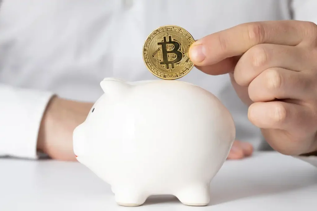 Bitcoin érme helyezése egy malacperselybe, ami a kriptovaluta befektetések megkezdését jelképezi.