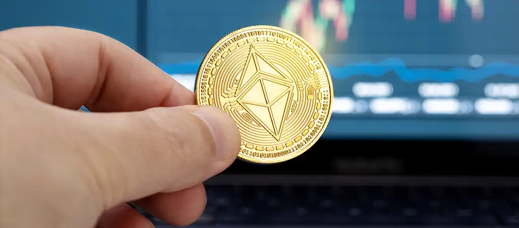 Ethereum érme kézben, élő árfolyam grafikon háttérrel