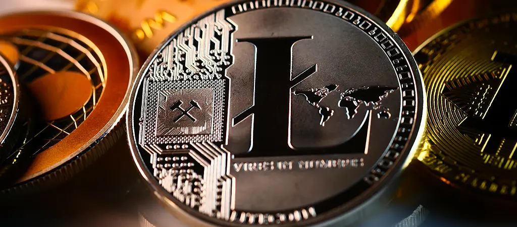 Ezüst színű Litecoin kriptovaluta érme közelről további népszerű kriptovaluta érmék mellett.