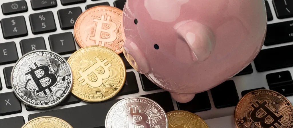Bitcoin érmék és rózsaszín malacpersely laptop billentyűzeten, kriptovaluta megtakarítás és befektetés.